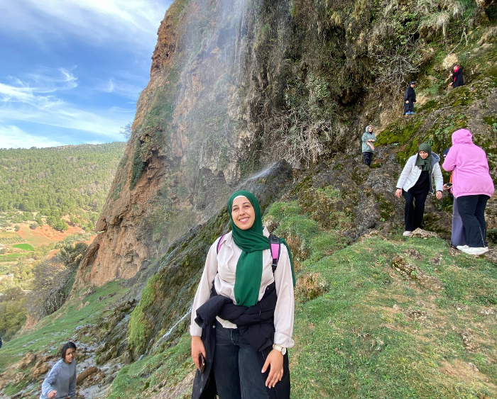 Zaynab hiking with a waterfall behind her